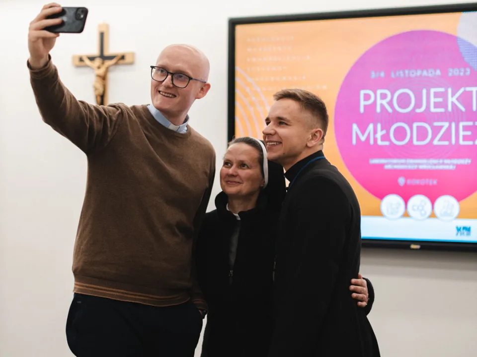 Troje ludzi robiących sobie zdjęcie na tle banery Projekt Młodzież